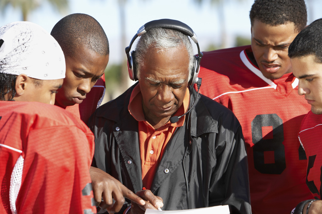 elderly male sports coach discussing with players in the field